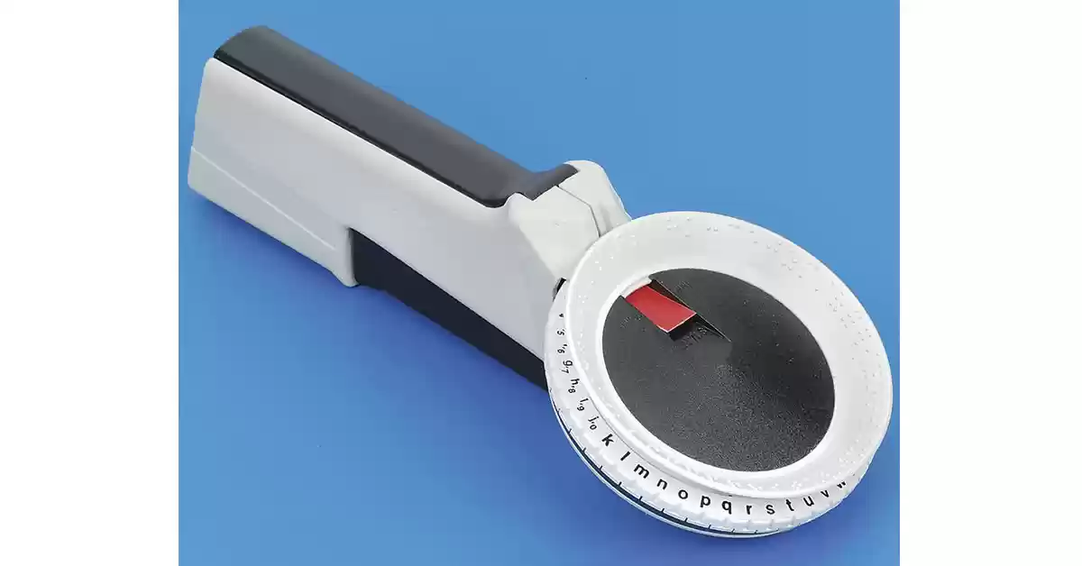 Pistola DYMO de escrita em Braille branca e preta com disco de correspondência do alfabeto a tinta.