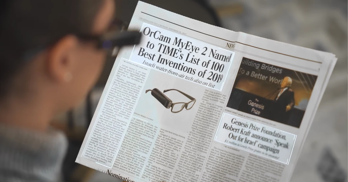 Senhora com o Leitor Orcam MyEye a fazer leitura de texto para voz num jornal