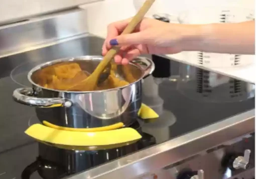 Duas guias amarelas em silicone amarelas a posicionar uma panela a cozinhar na placa de indução.